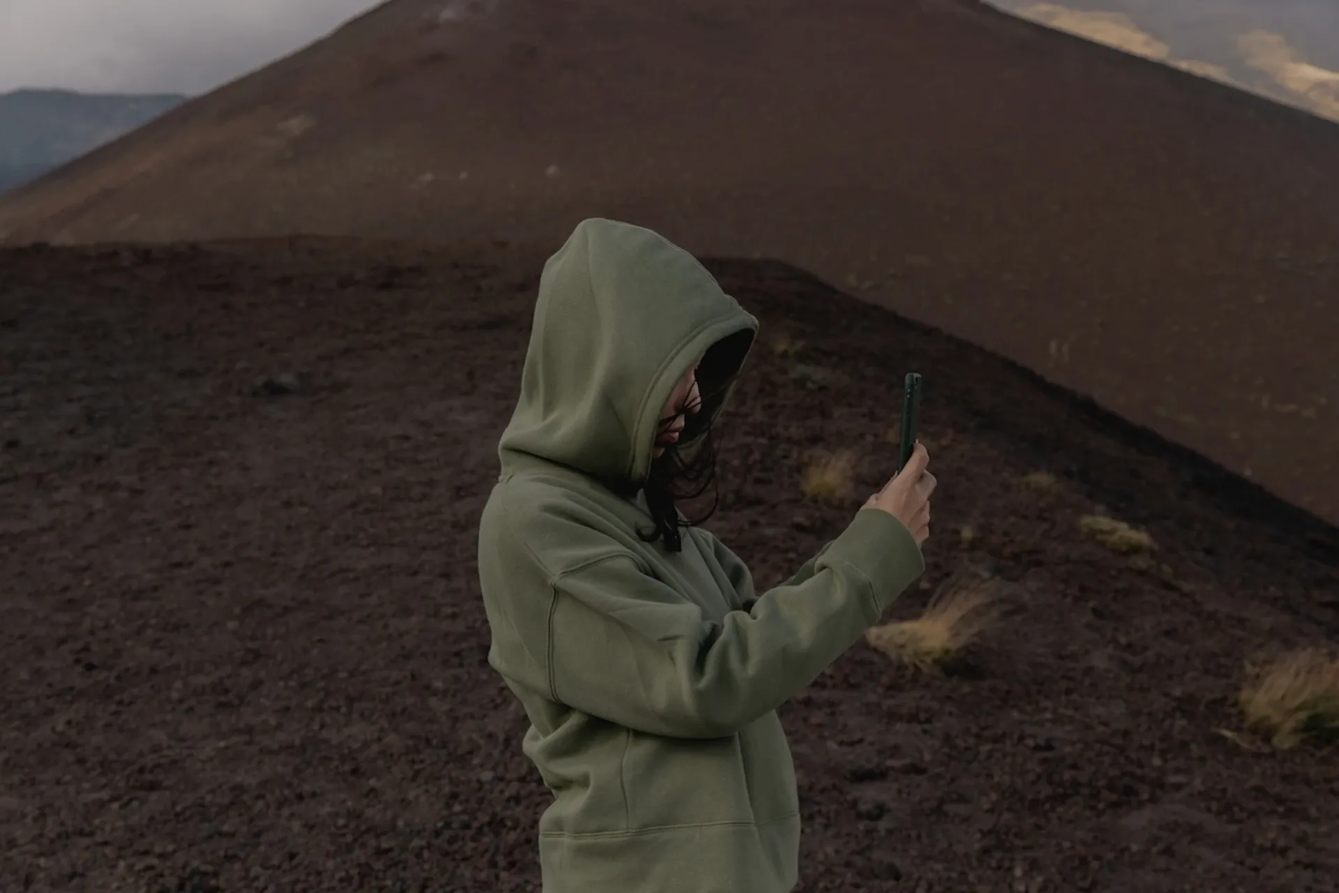 Person taking a photo while stood on a black, sandy hill