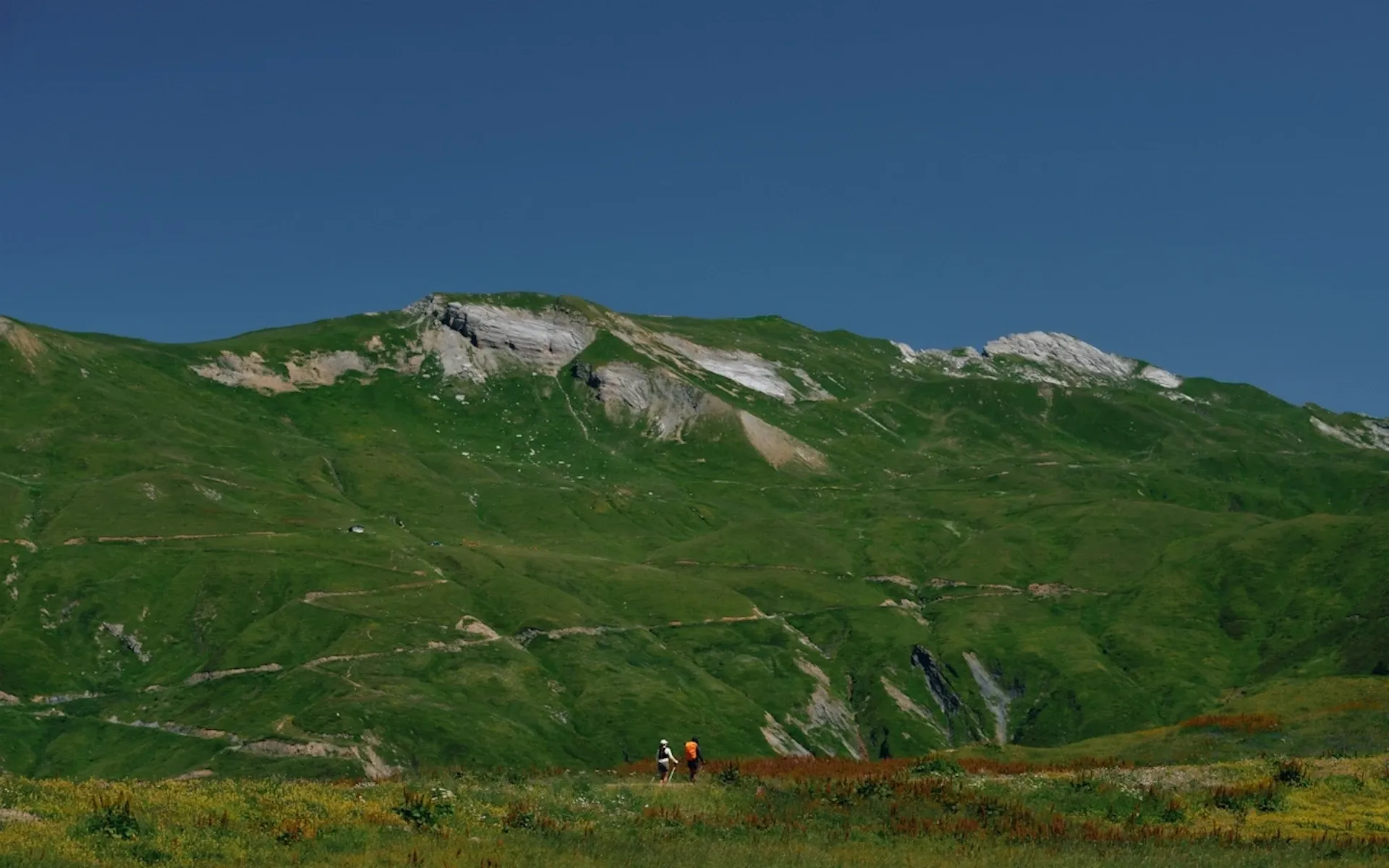 A mountain range on a sunny day, with two hikers walking past