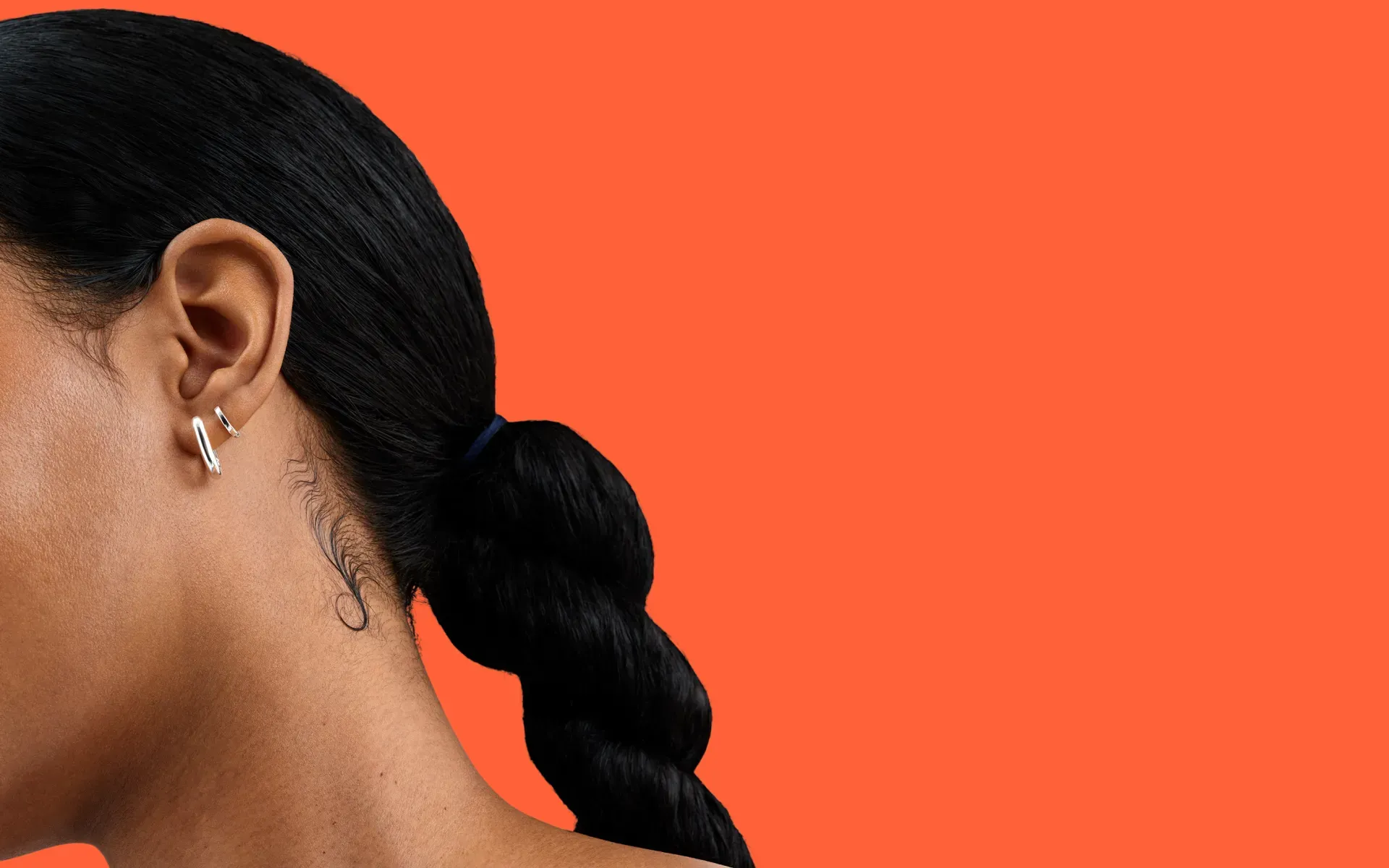 Close-up shot of a person’s neck and hair. They are wearing two gold earrings