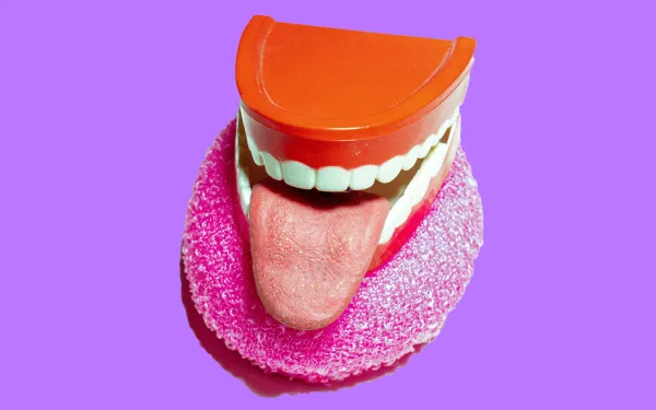 A tongue sticking from a pair of false teeth, on top of a donut